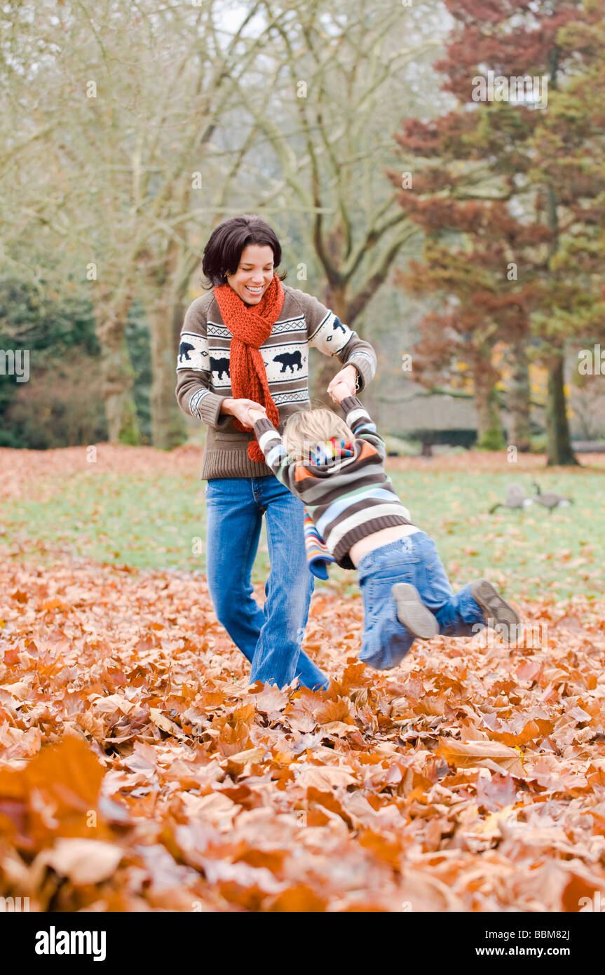 Mamá columpios hijo alrededor en hojas de otoño, Vancouver, British Columbia Foto de stock