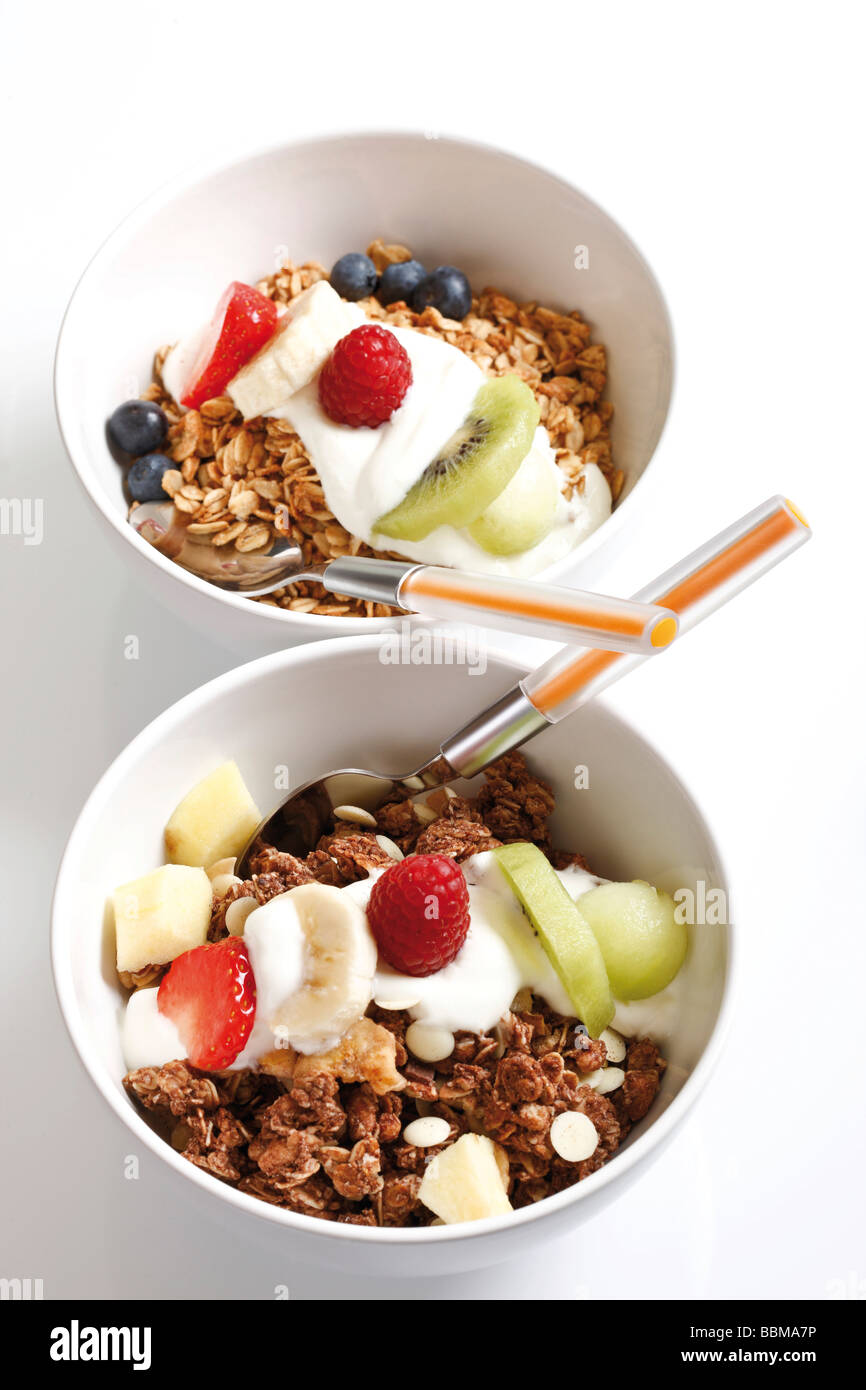 Muesli con yogur y fruta en cuencos de porcelana, kiwi, frambuesa, fresa y arándanos Foto de stock