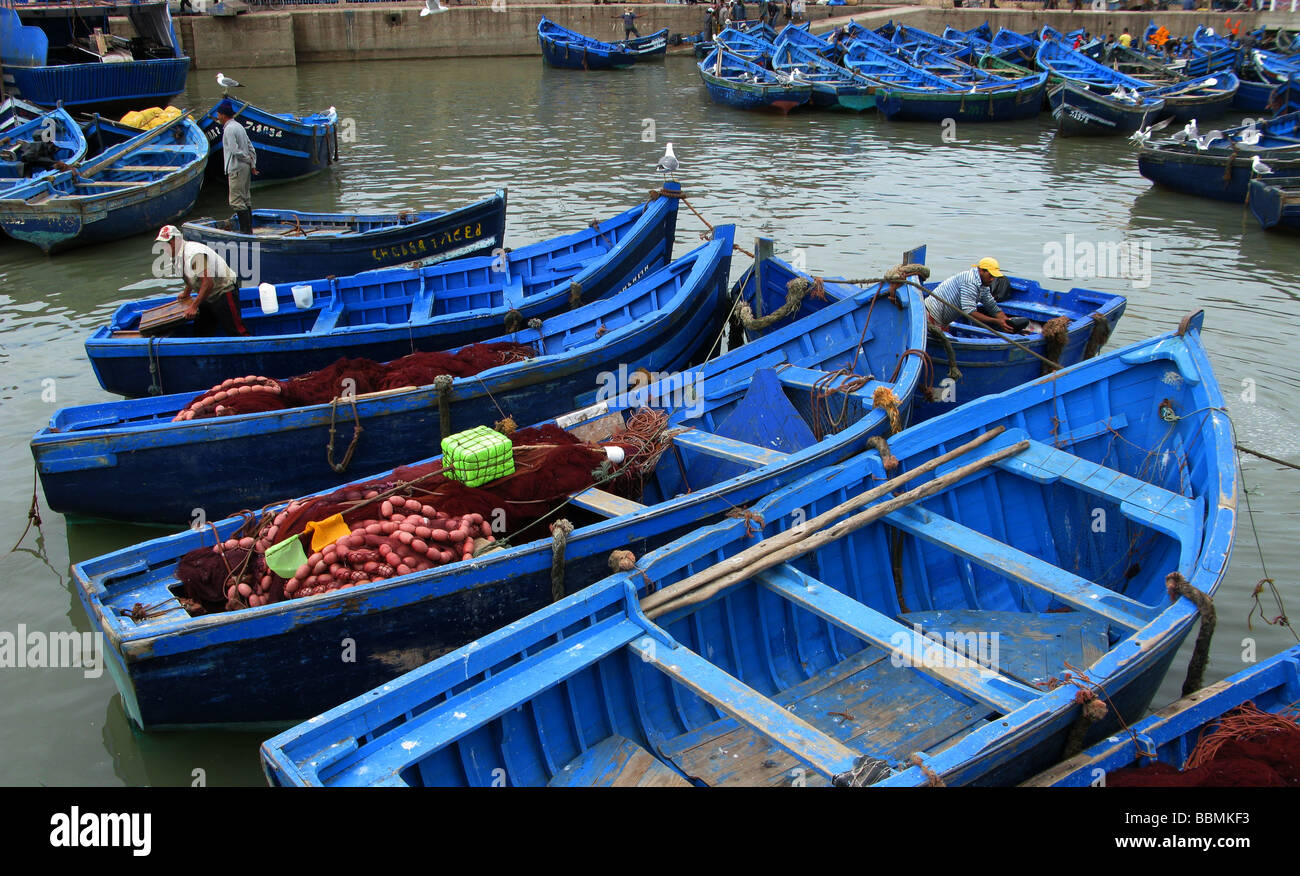 Los pescadores, en el puerto, arreglando las redes. Los buques de pesca que  van al mar en el muelle, el azul del mar se refleja en la pintura  Fotografía de stock -