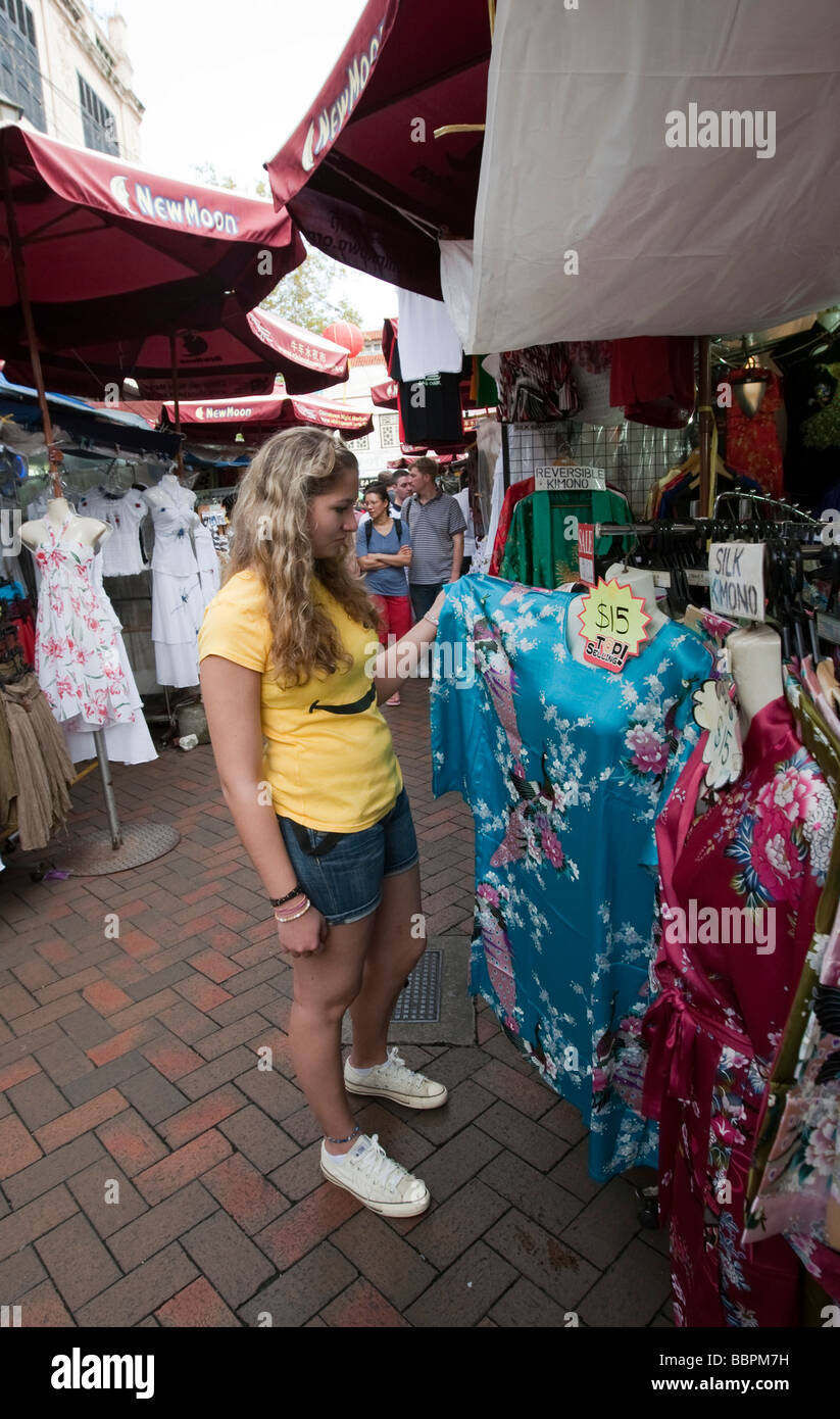 Turista está interesado en un vestido, Chinatown, el colorido mercado como una atracción turística, la calle Temple Street, Singapur, Sudeste de Asia Foto de stock