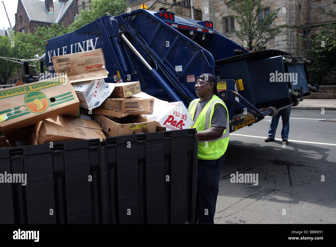 Un hombre se prepara para mover un contenedor lleno de cartón reciclables en un camión recolector de basura en la Universidad de Yale en New Haven CT USA Foto de stock