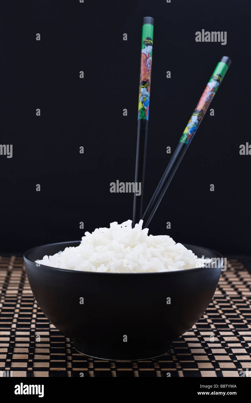 Arroz blanco cocido en negro plato con dos palillos chinos Foto de stock