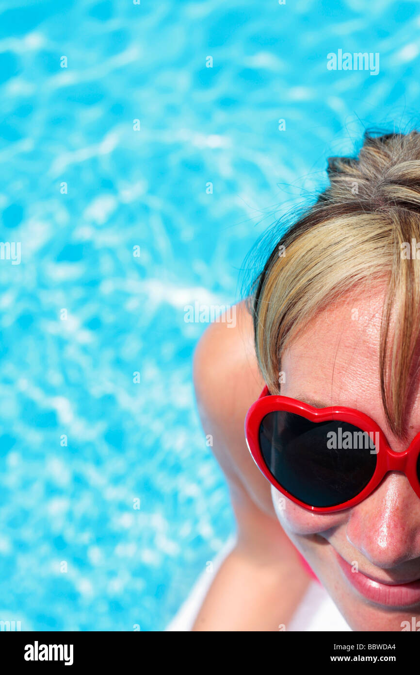 Mujer con gafas de sol en forma de corazón, además de una piscina azul brillante Foto de stock