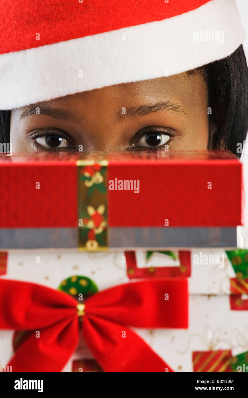 Mujer Africana vistiendo traje de Santa peeking a través de regalos de Navidad Foto de stock