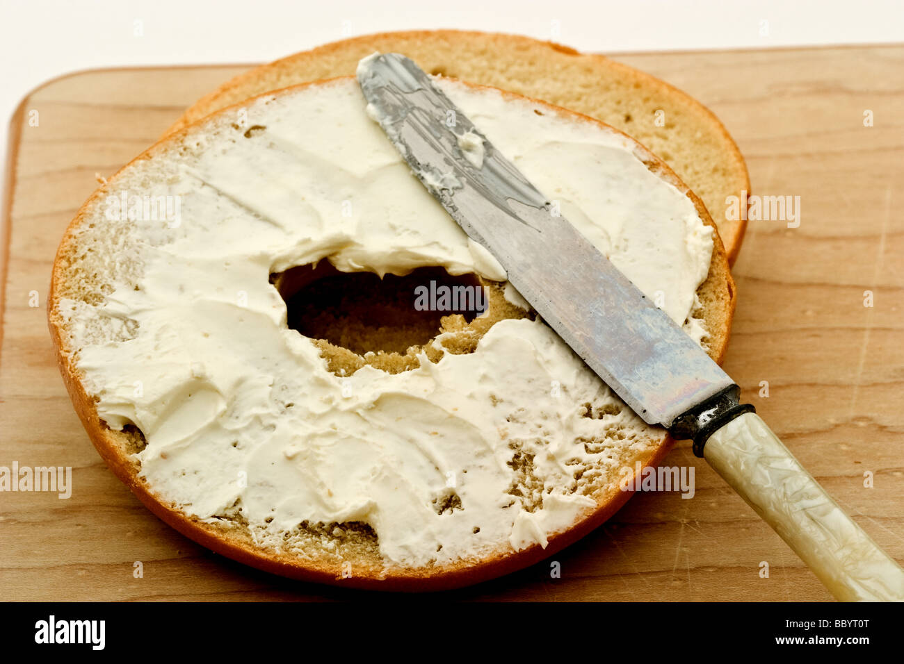 Bagel con crema de queso con un cuchillo sobre una tabla para cortar Foto de stock