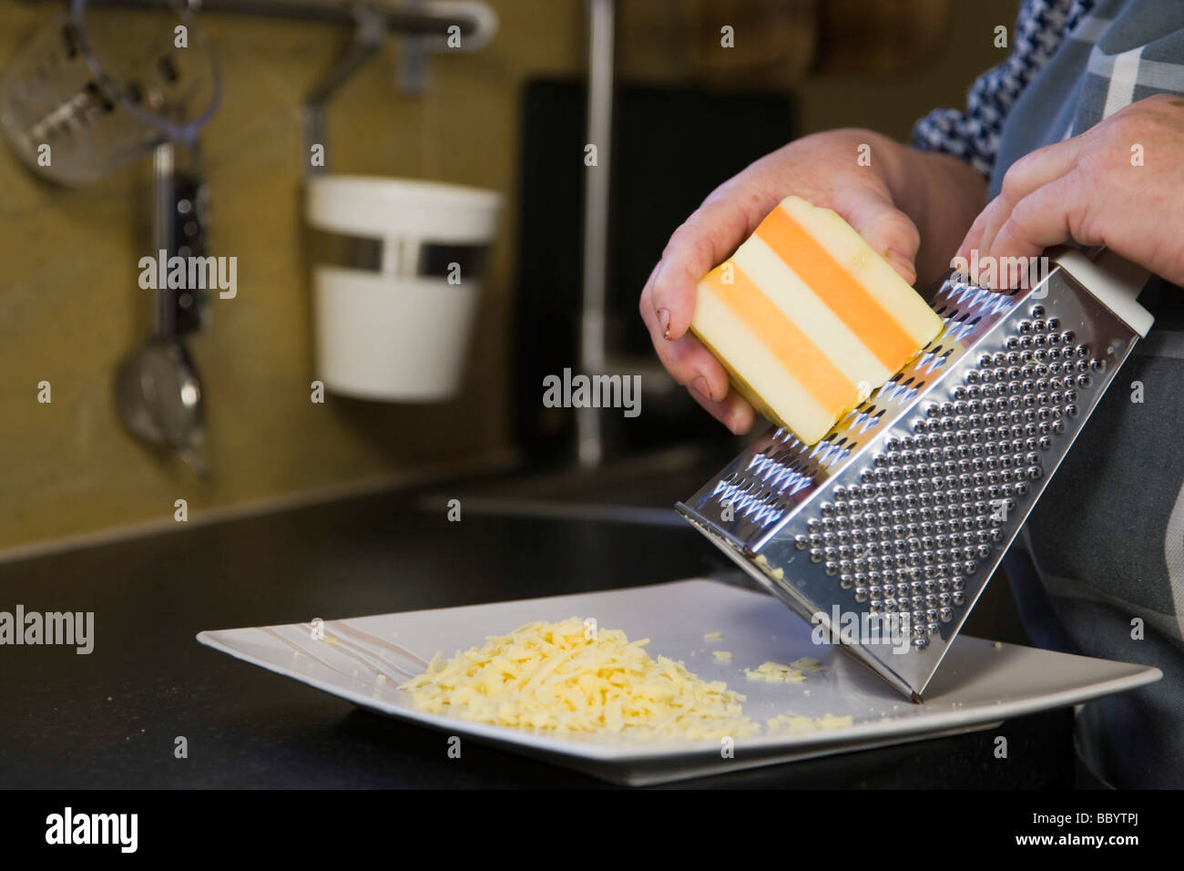 Manos de mujer, 67 años, rallar queso en la cocina Foto de stock