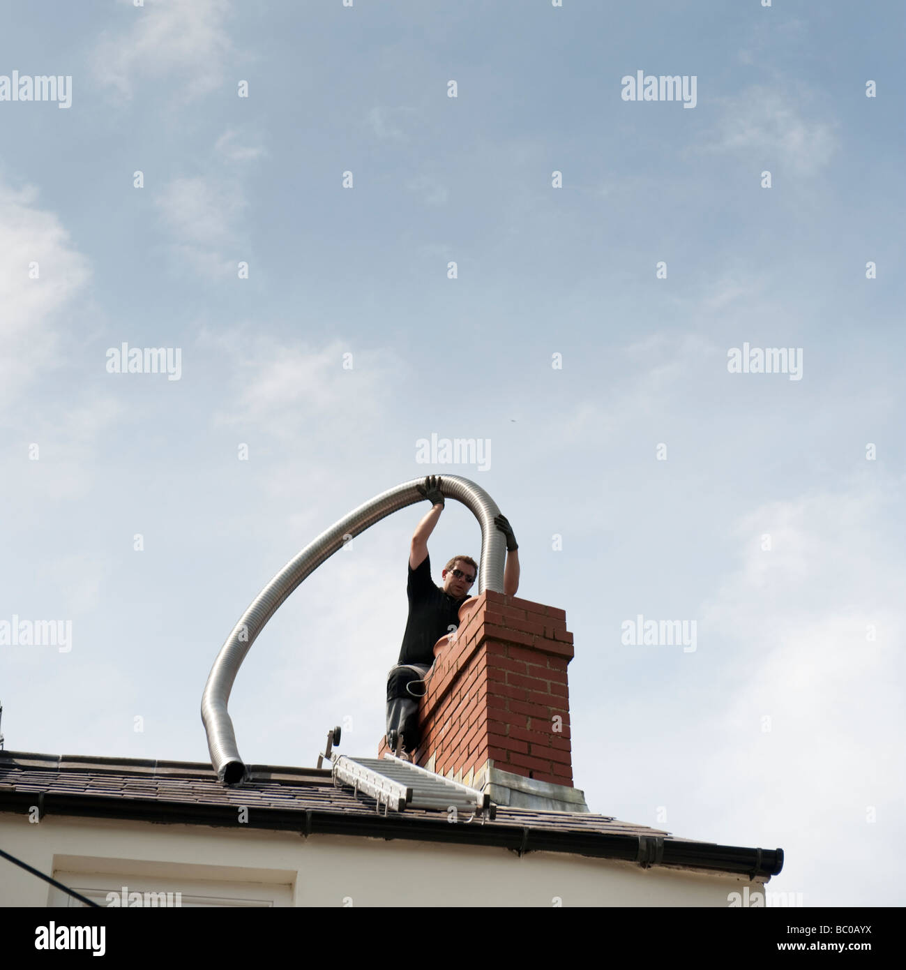 Un hombre de metal flexible instalación de chimenea flue liner a una casa en el pequeño refugio Gales pembrokeshire UK Foto de stock