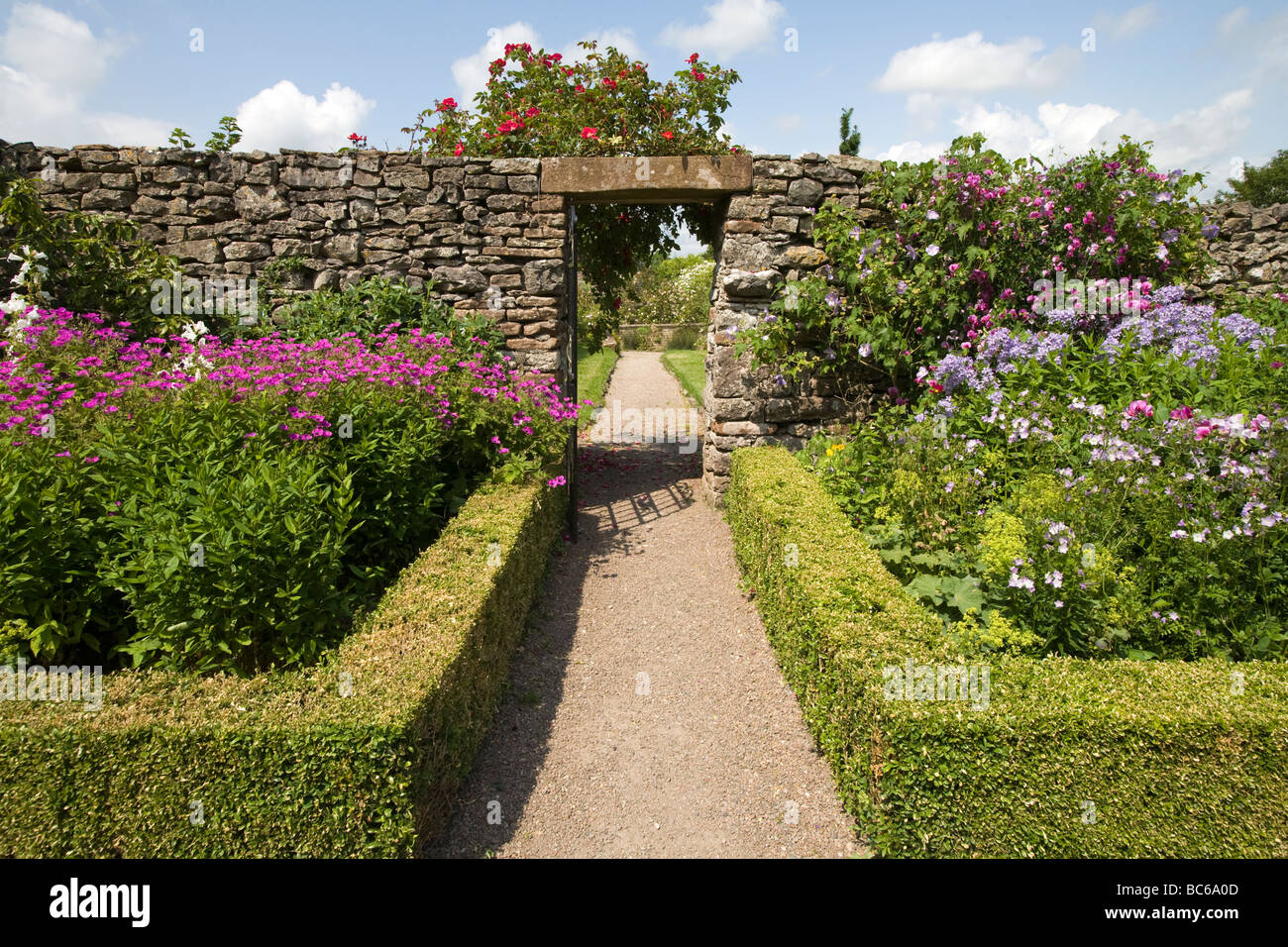Jardín camino bordeado con baja cobertura de cuadro de flores y arbustos y apertura en muro de piedra seca English country garden UK Foto de stock