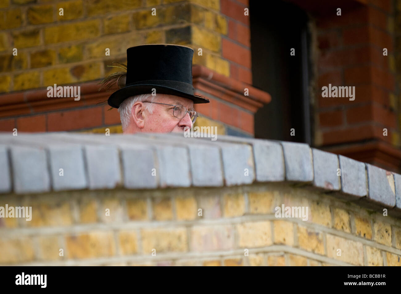 Un hombre que llevaba un sombrero superior mirando por encima de una pared en Essex. Foto de stock