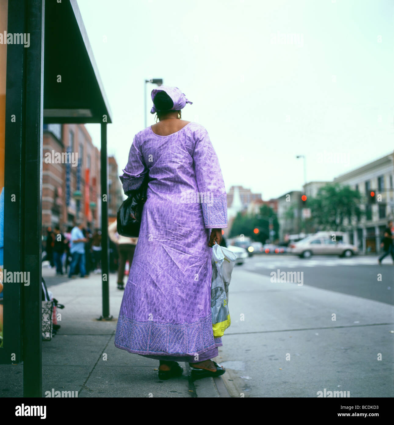 Vista posterior del textil africana sobre la mujer esperando en una parada de autobús en Harlem vistiendo un traje morado comprados en África en la Ciudad de Nueva York, EE.UU. Kathy DEWITT Foto de stock