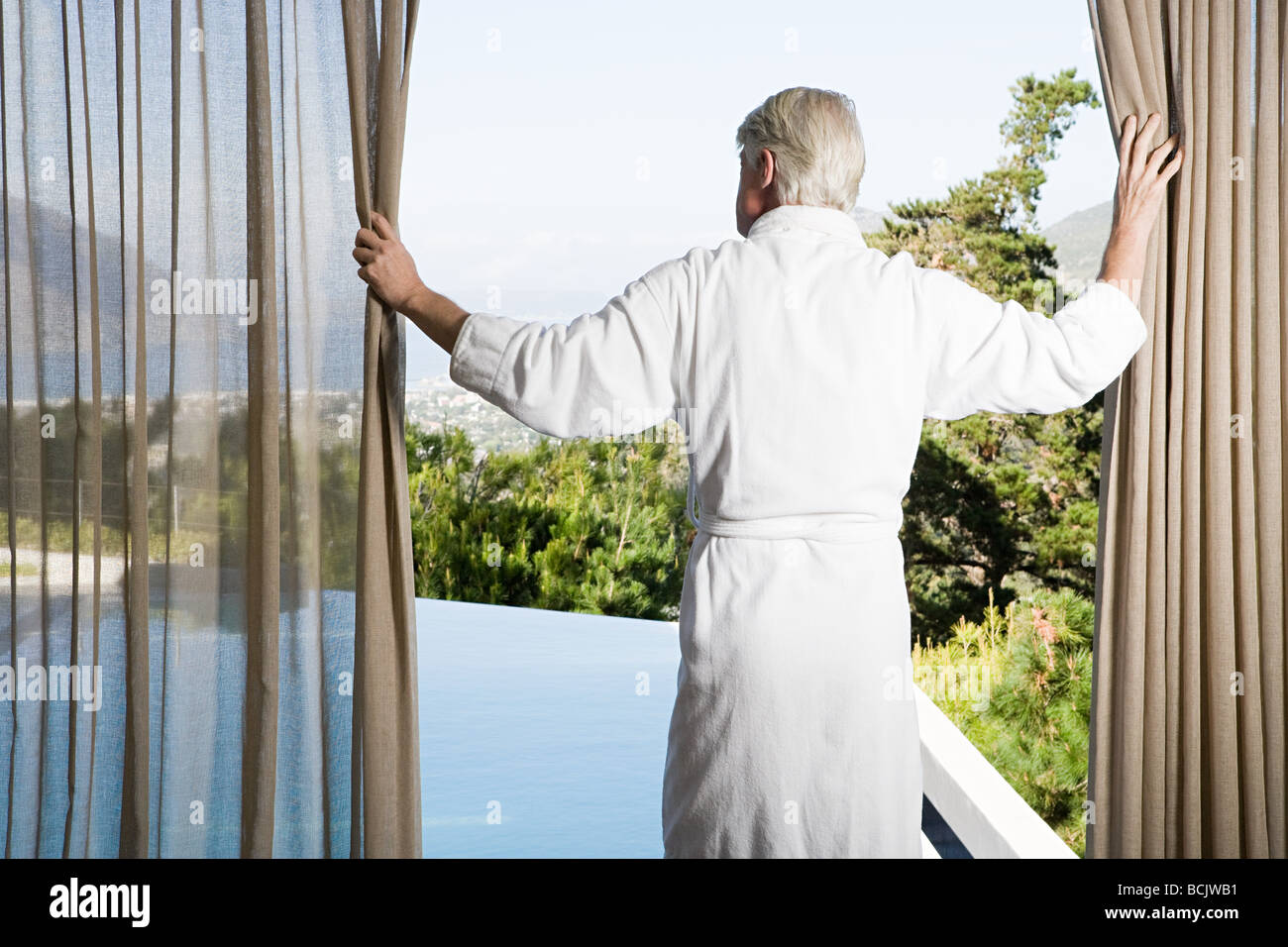 Hombre de mediana edad vistiendo albornoz tirando cortinas en frente de la  piscina Fotografía de stock - Alamy