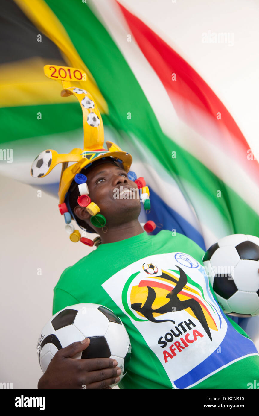 Joven vistiendo un tradicional soccer Makaraba y celebración de balones de fútbol con la bandera de Sudáfrica Foto de stock