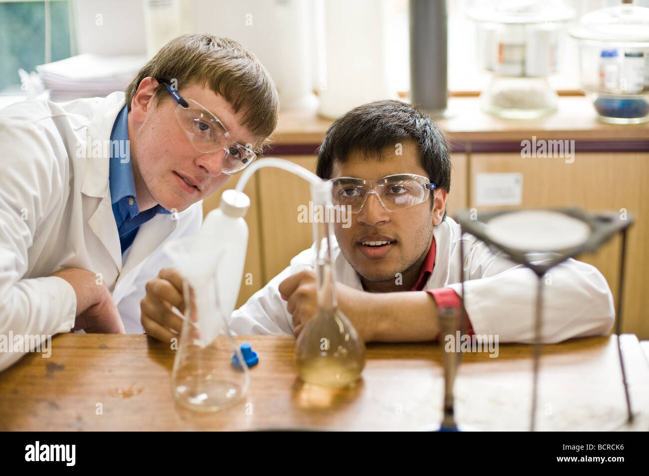 Escuela británica Inglaterra Educación de la Escuela Gramática - dos estudiantes varones que derraman líquido en un experimento en un laboratorio de ciencias de la escuela. Foto de stock