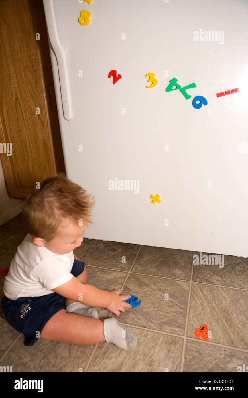 Un año viejo muchacho recogiendo letra del alfabeto imanes y ponerlos de nuevo en el refrigerador Foto de stock