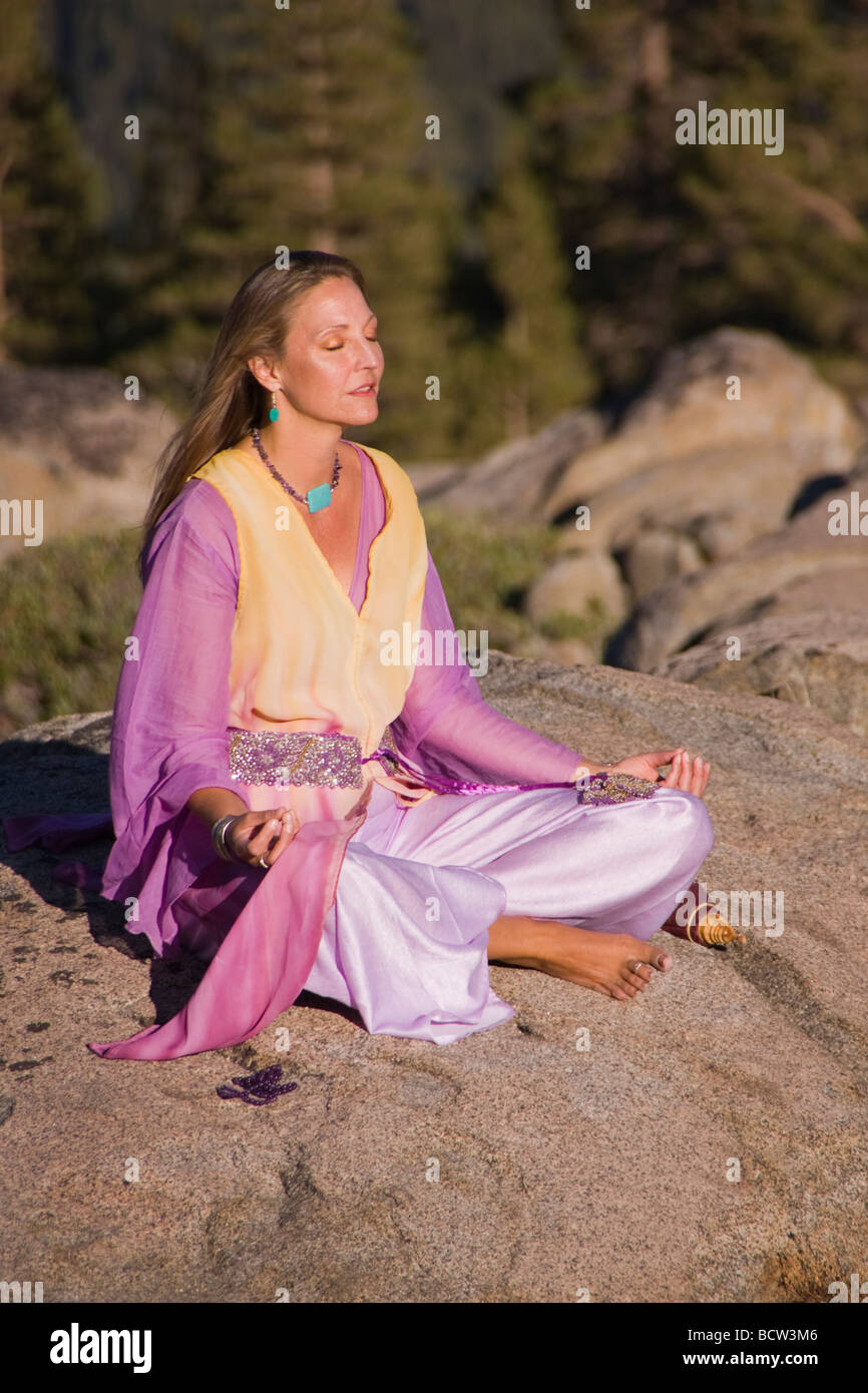 Mujer madura en ropas ostentosas meditando sobre una roca Foto de stock