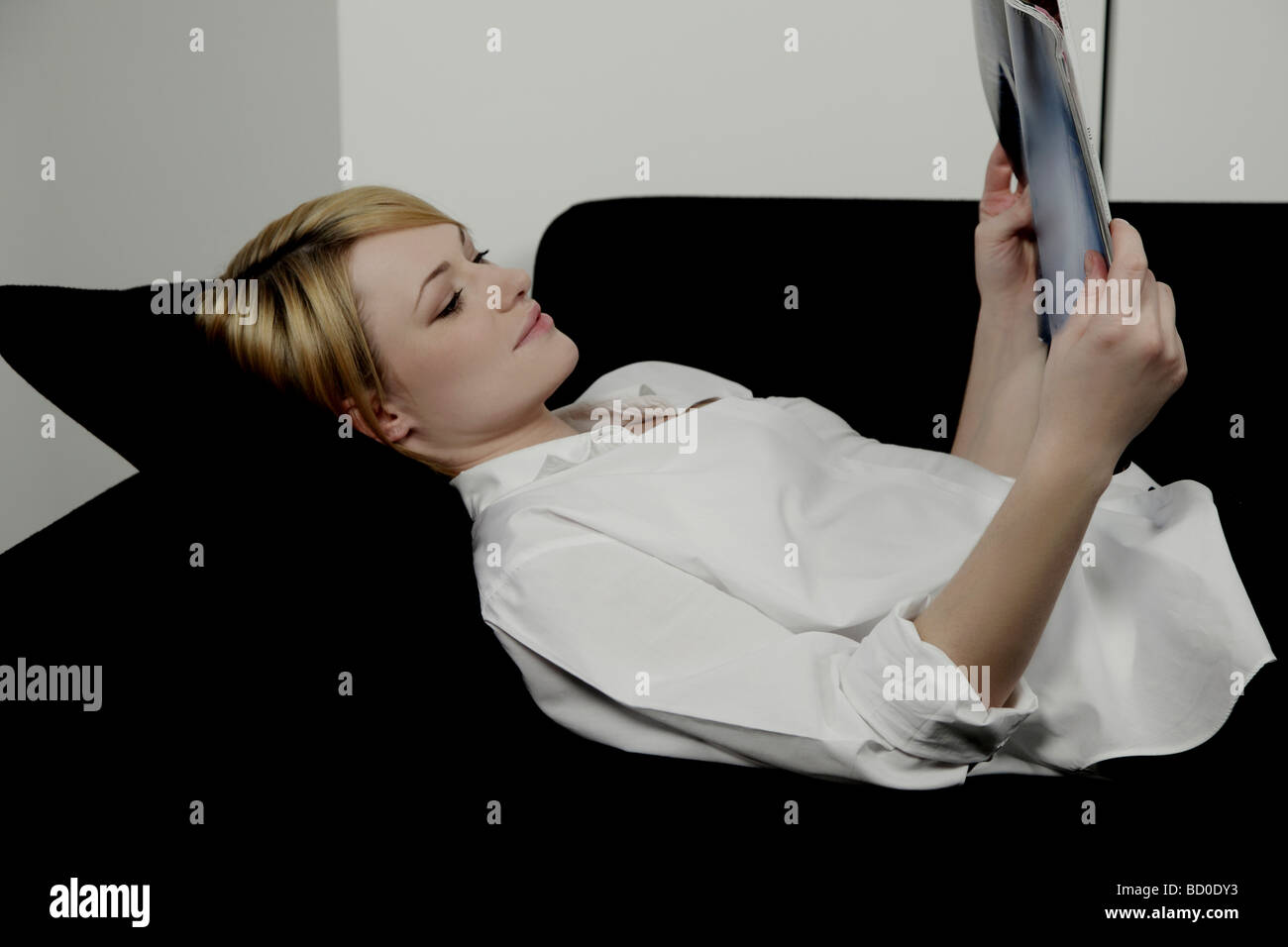 Mujer recostada sobre un sofá leyendo la revista. Foto de stock