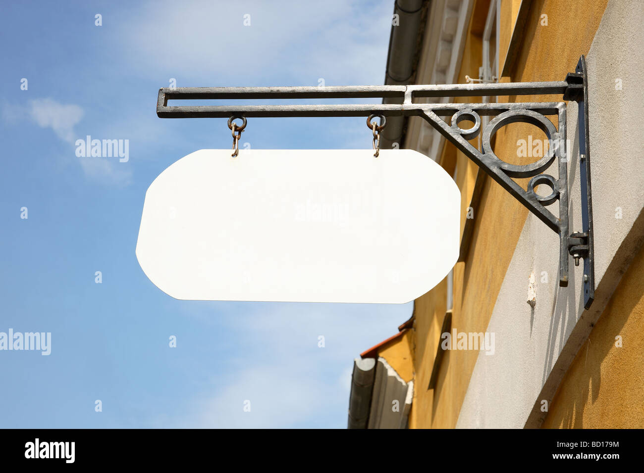 Blanco, blanco shop cartel colgado en un soporte de hierro forjado sobre  una pared amarilla contra un cielo azul Fotografía de stock - Alamy