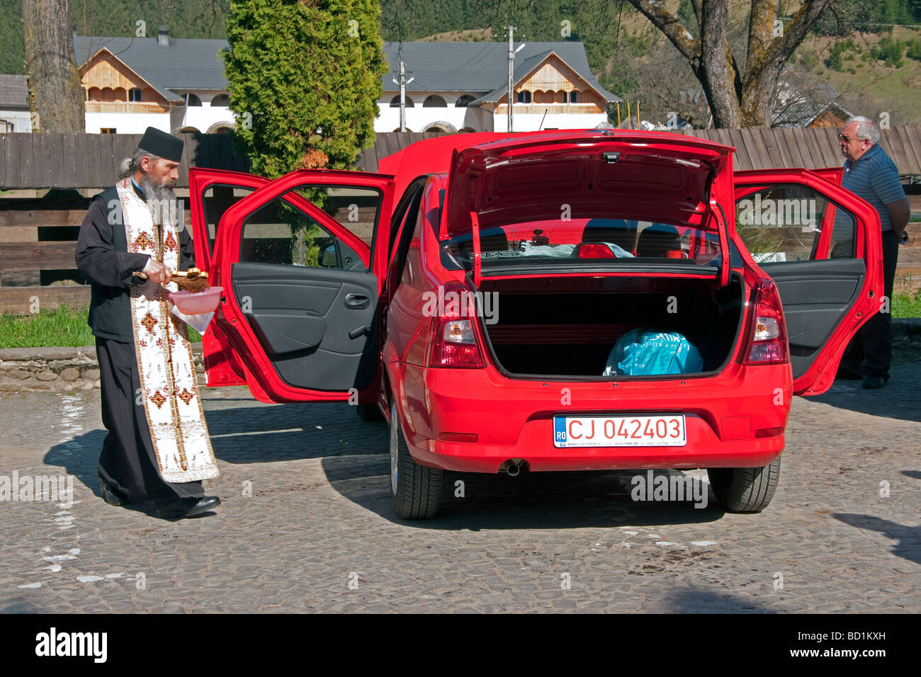 Sacerdote ortodoxo rumano bendición nuevo Dacia auto con agua bendita a su propietario en el Condado de Maramures, en el norte de Transilvania Foto de stock