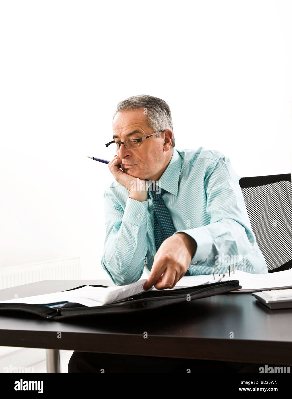 Manager con gafas, sentado en su escritorio con un ordenador y un concentratedly estudiando sus documentos Foto de stock