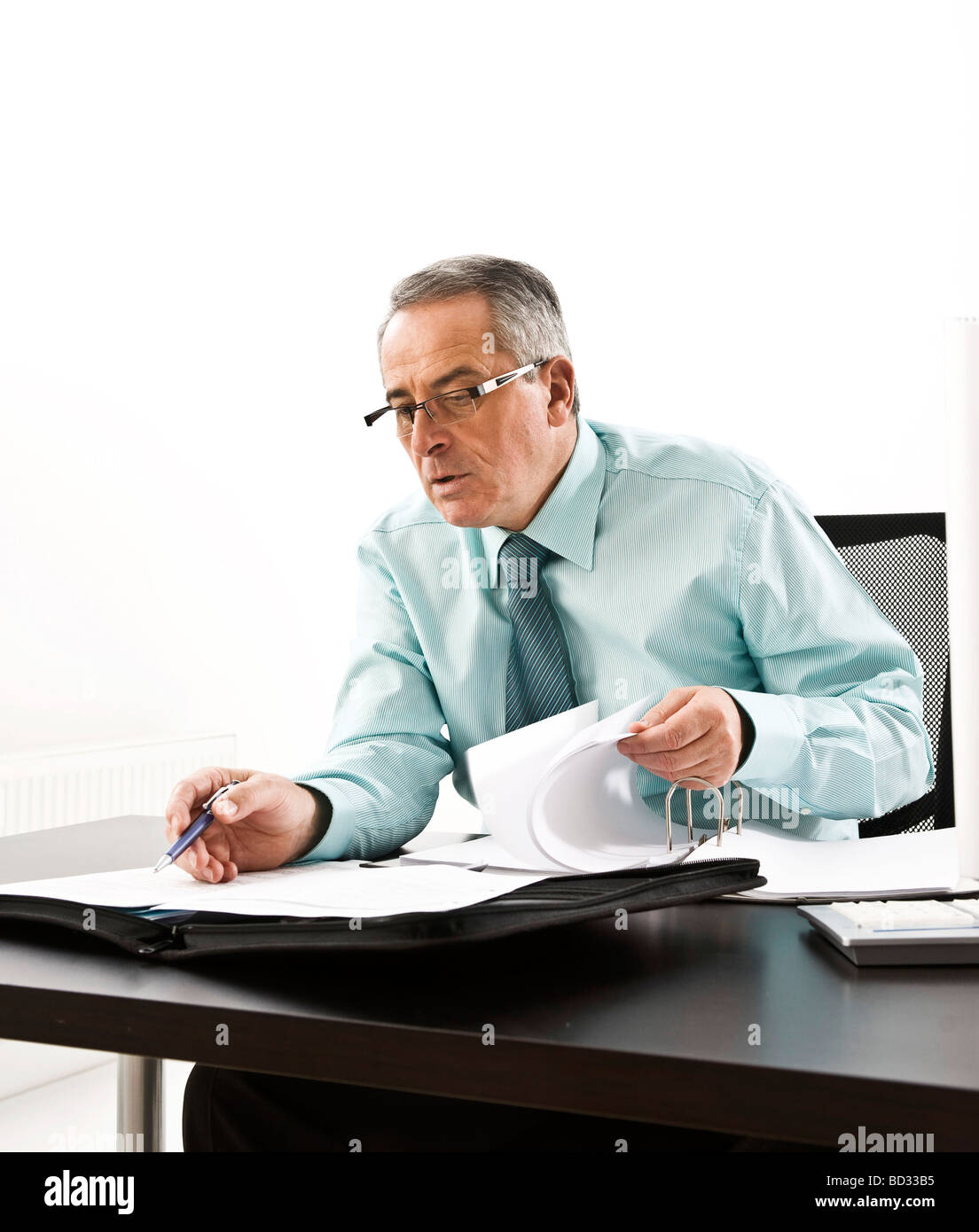 Manager con gafas, sentado en su escritorio con un ordenador y un concentratedly estudiando sus documentos Foto de stock