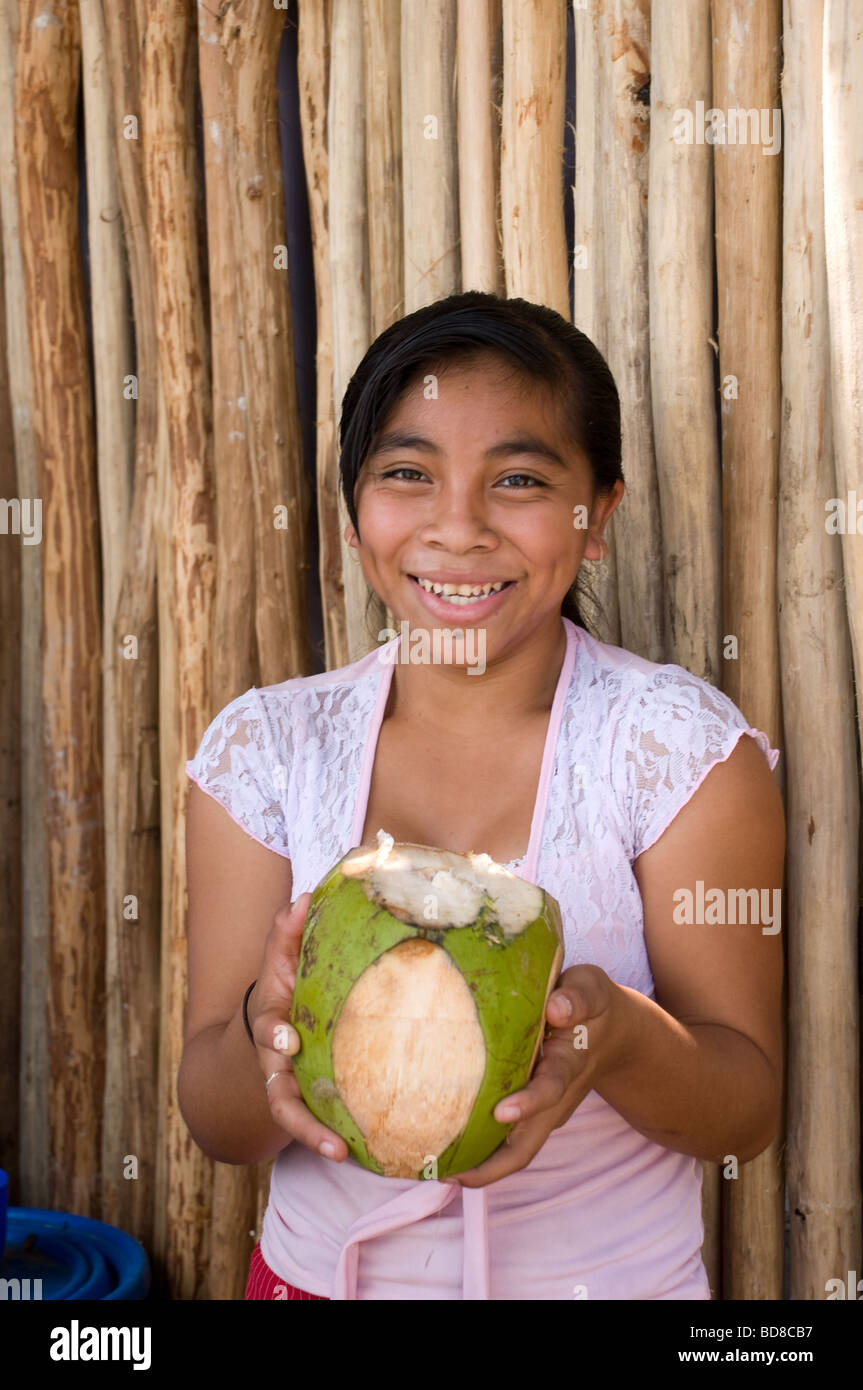 Un feliz niña mexicana ofrece y coco helado para la venta a los turistas que visitan Chichén Itzá. Foto de stock
