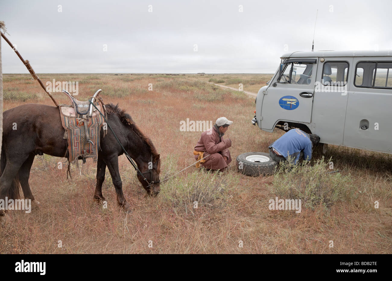 Contrastando los medios de transporte: un jinete mongol supervisa las reparaciones del vehículo, al norte de Mongolia central. Lo que es más fiable? Foto de stock