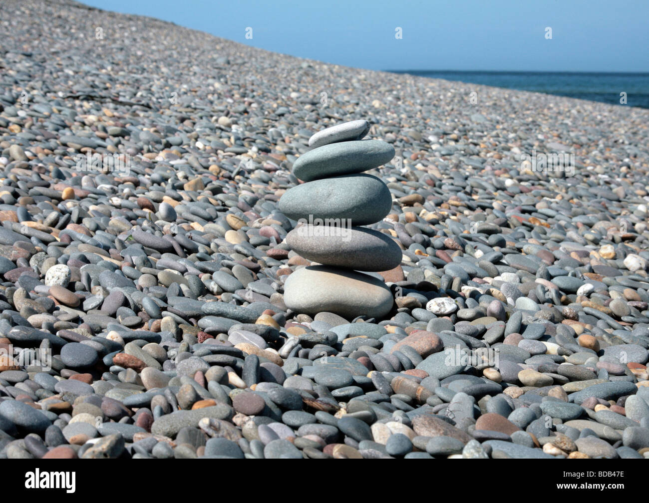 5 piedras apiladas en una playa de guijarros, vislumbrar el azul del cielo y del océano Foto de stock
