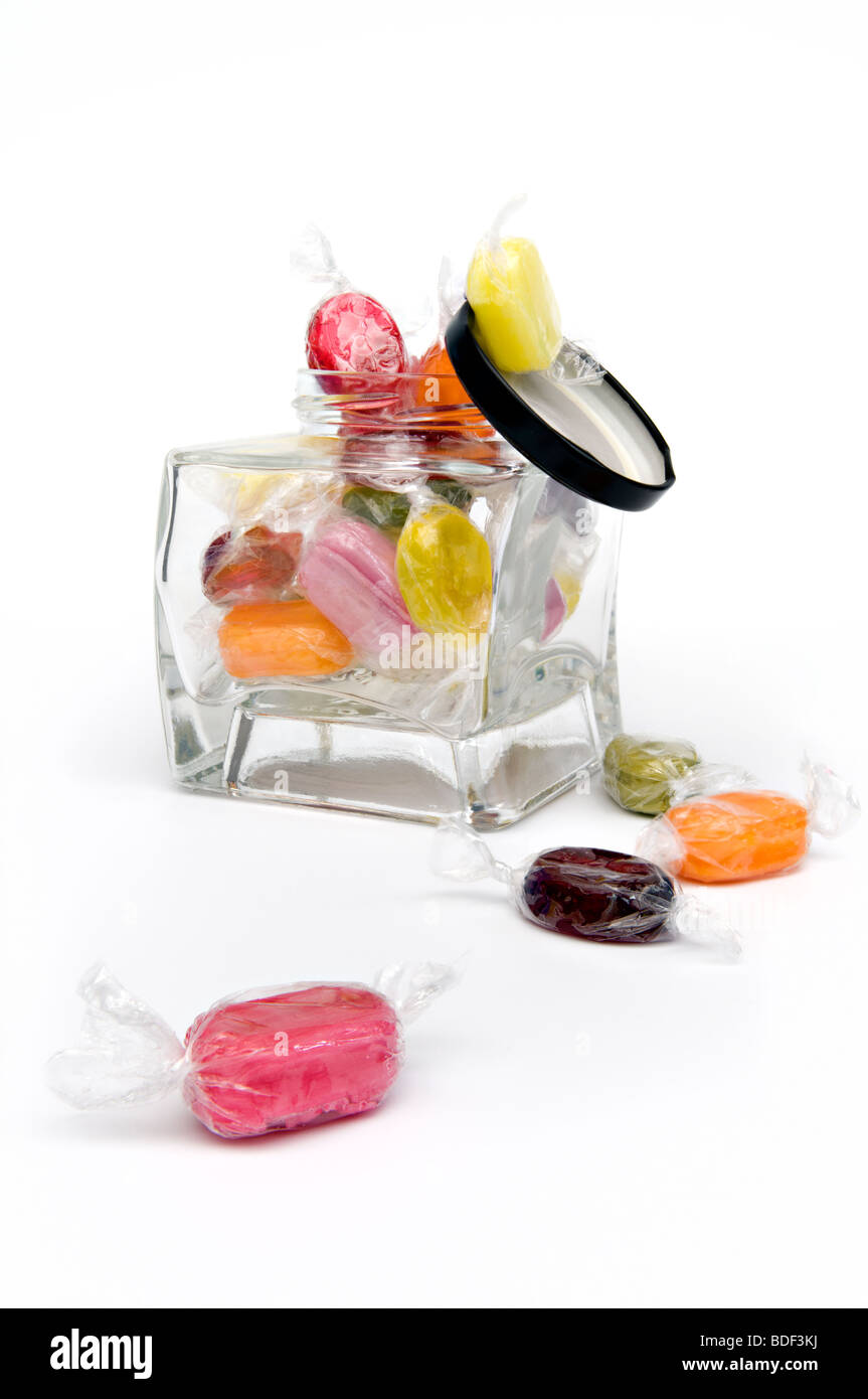 Foto de estudio de hervido dulces afrutados en abrir un tarro de vidrio contra un fondo blanco con tapa cayéndose Foto de stock