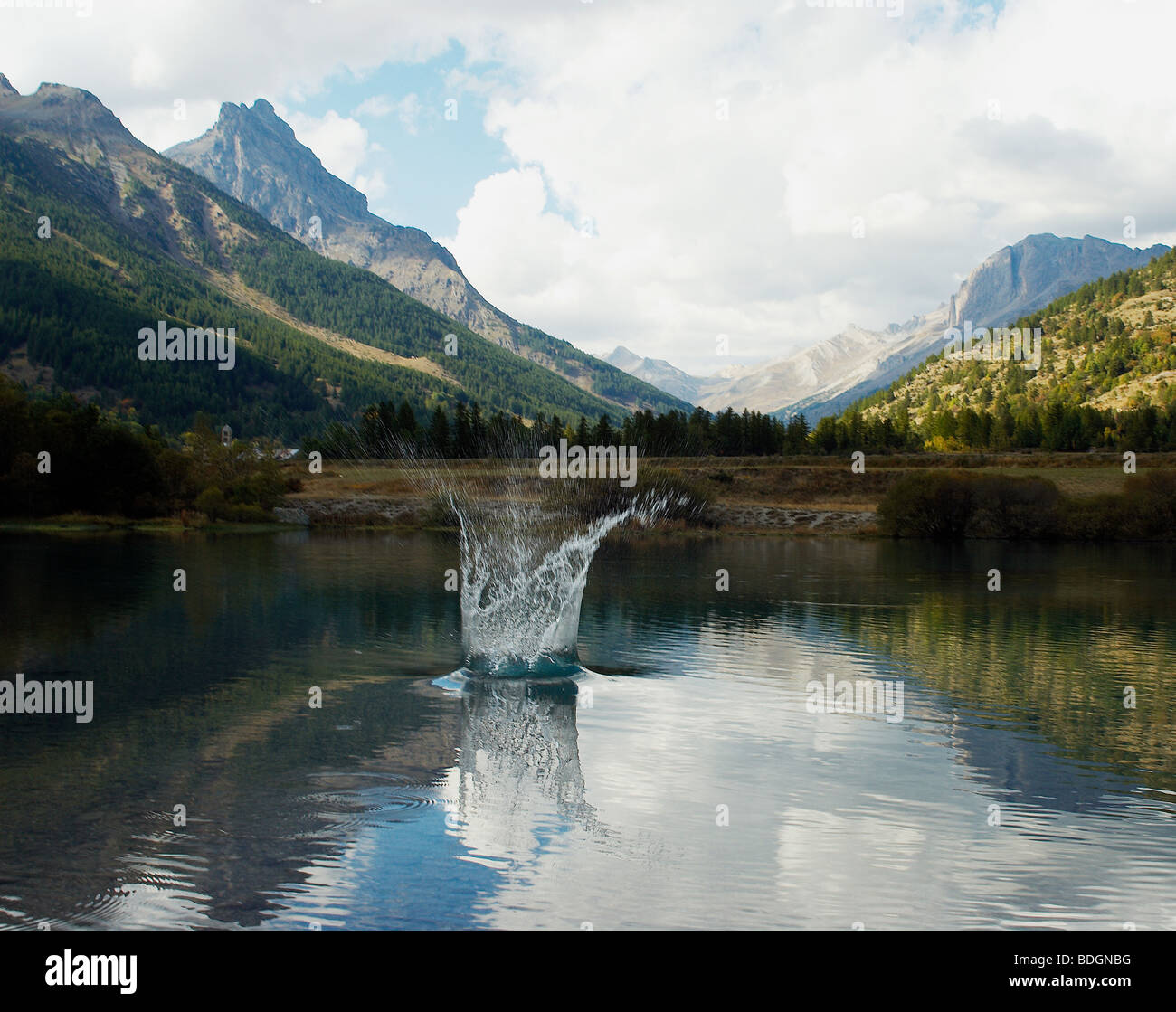 Una vista de los Alpes, con un lago en el primer plano. un chorrito de agua saltando desde el lago Foto de stock