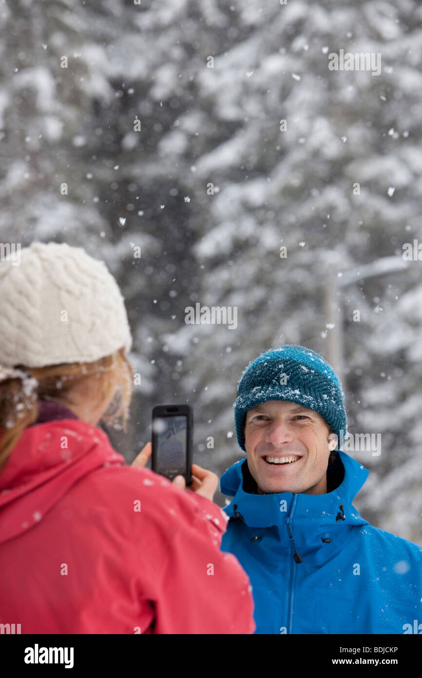 Mujer toma la imagen del hombre con la cámara del teléfono al aire libre en invierno, Whistler, British Columbia, Canadá Foto de stock