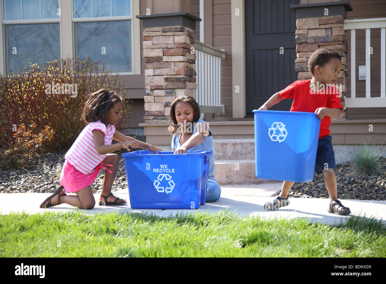 Tres niños colocando elementos en la papelera de reciclaje Foto de stock