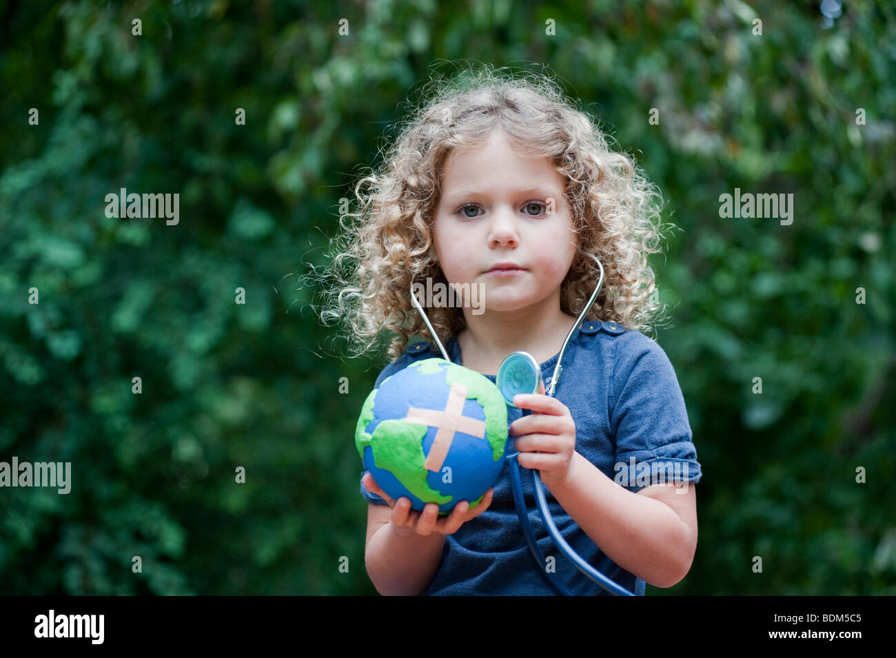 Joven sosteniendo un modelo de un planeta enfermo con una Curita" adjunto y controlar su salud con un estetoscopio Foto de stock