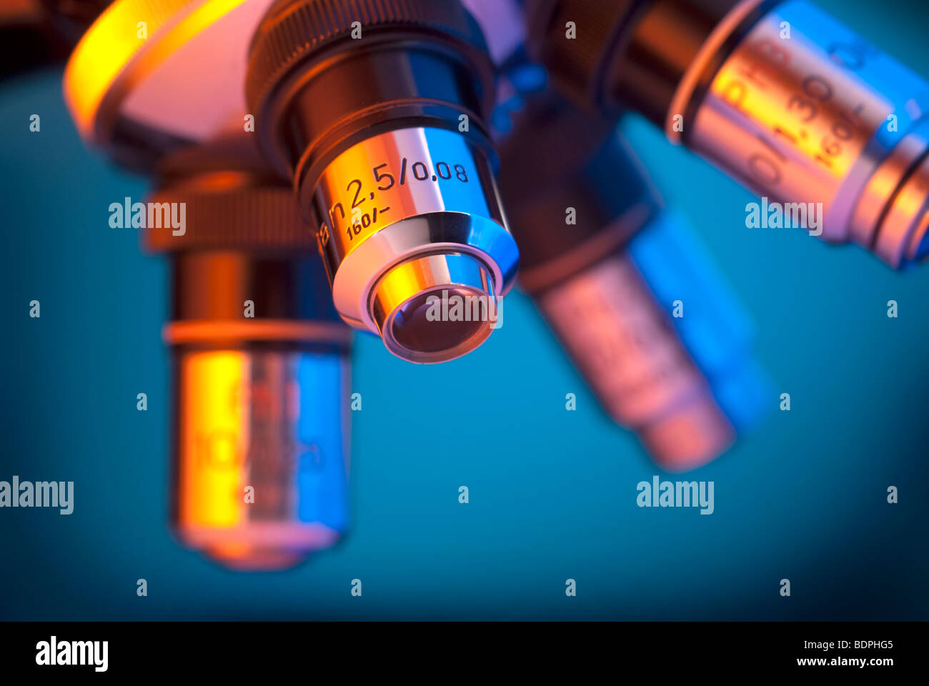 Cerca de cuatro lentes clásicas torreta del microscopio iluminado por luces naranja y cian Foto de stock