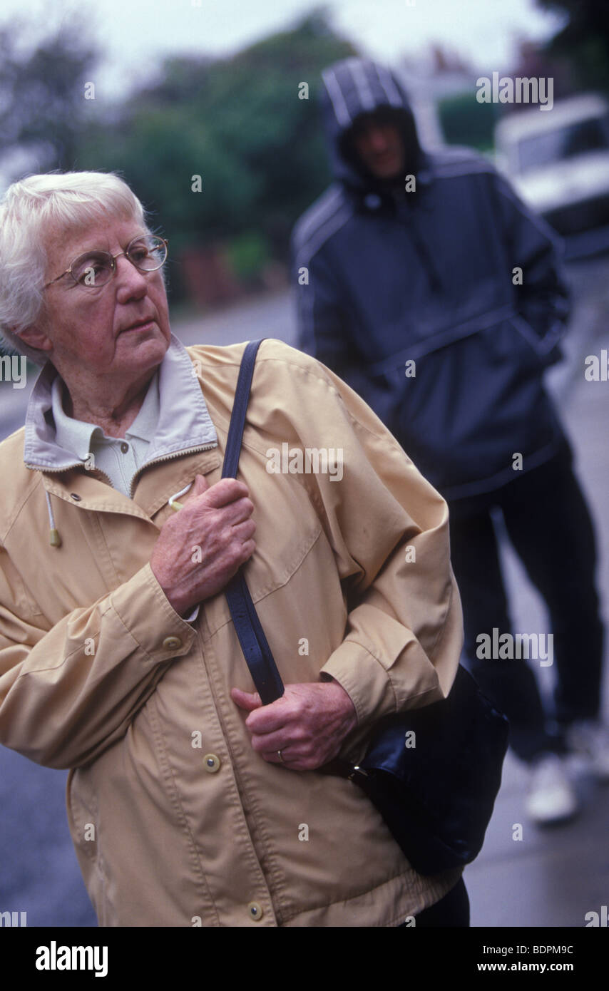 Anciana busca preocupado mientras era seguido por un hombre de aspecto agresivo en un capó Foto de stock