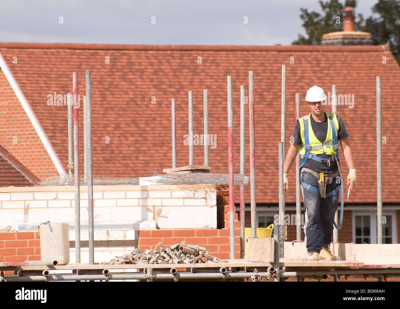Un trabajador de la Construcción de Andamios caminando a través de la plataforma por una casa en construcción. Foto de stock