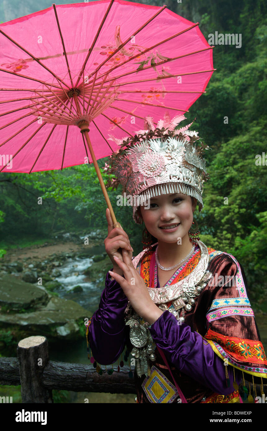 Chica guapa posando en traje Tujia formal sosteniendo paraguas rosa para fotos Wulingyuan Scenic Parque Nacional de la provincia de Hunan en China Foto de stock