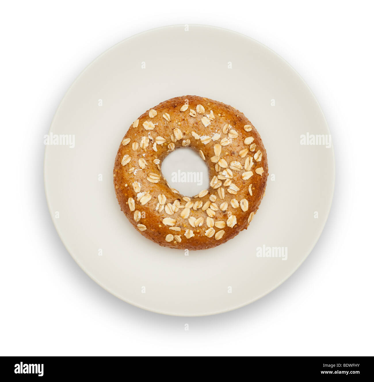 Un grano entero bagel en una placa blanca, aislado sobre fondo blanco. Guarda con trazado de recorte. Foto de stock