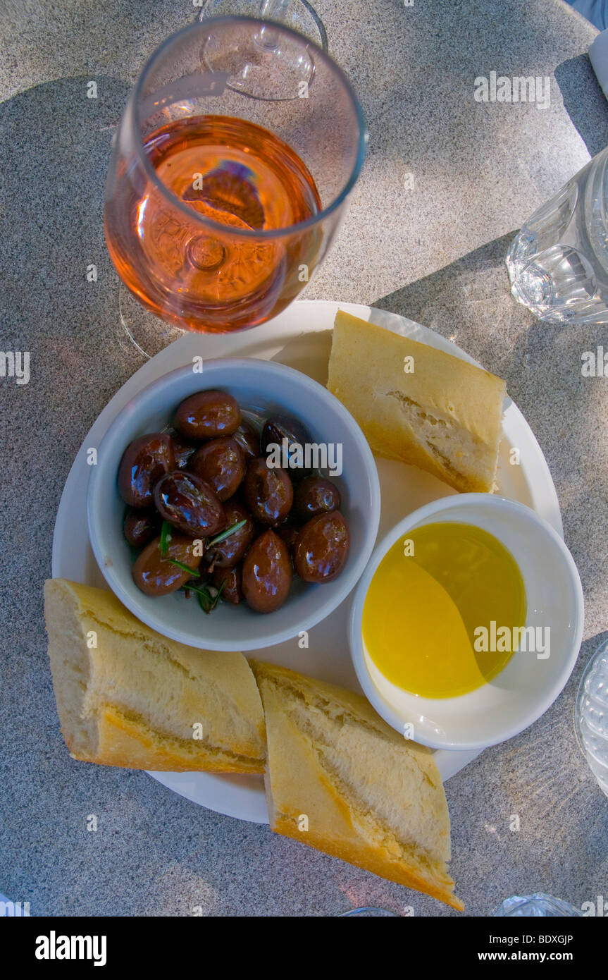 Un aperitivo de aceitunas cultivadas orgánicamente, aceite de oliva y crujiente pan con un vaso de rosa Foto de stock