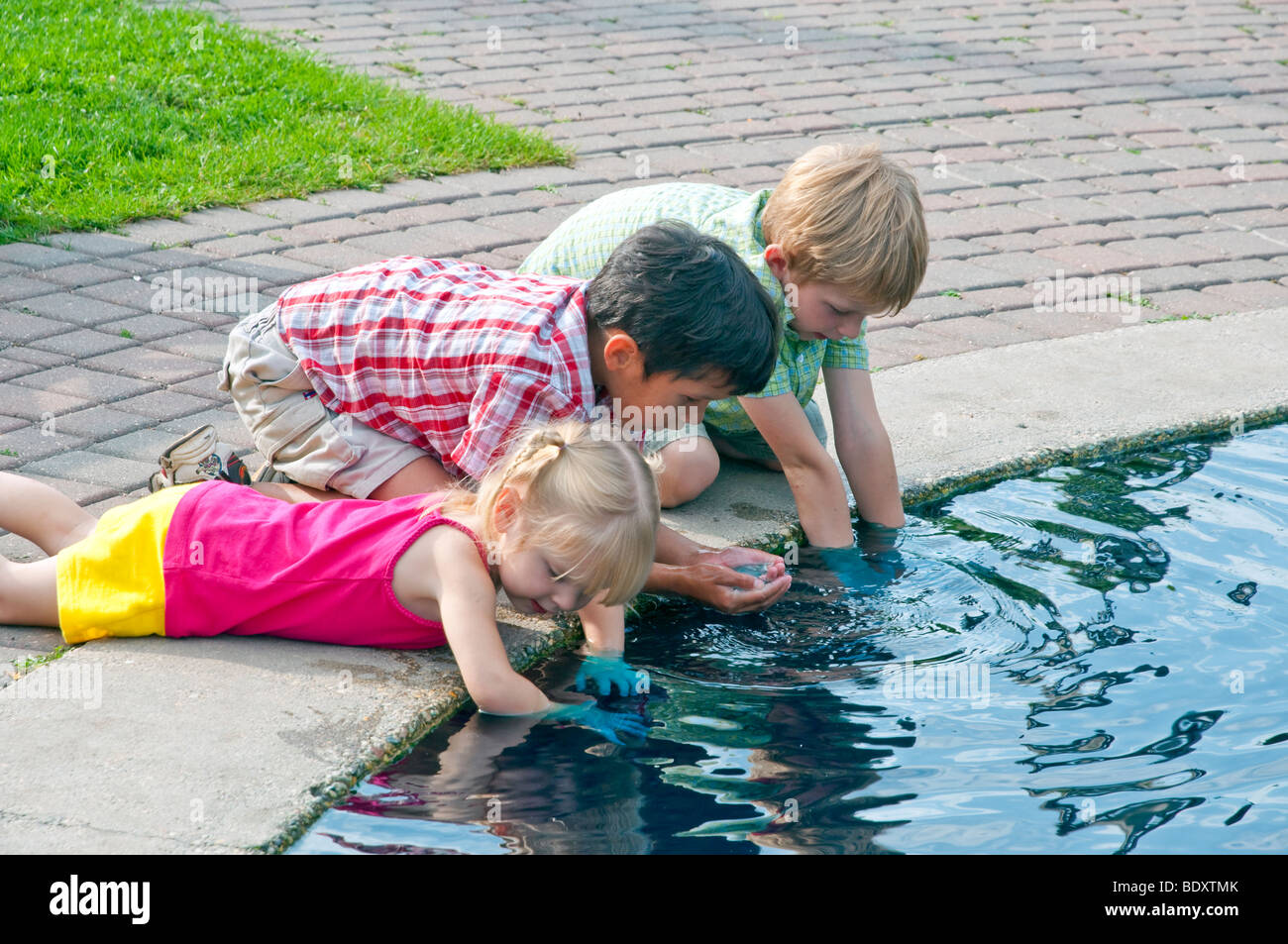 Tres niños con sus manos en el agua jugando en una piscina ...