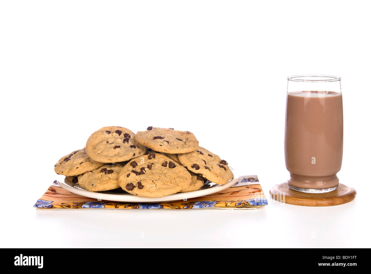 Un plato lleno de galletas con trocitos de chocolate casero con un frío vaso de leche con chocolate listo para consumir. Foto de stock