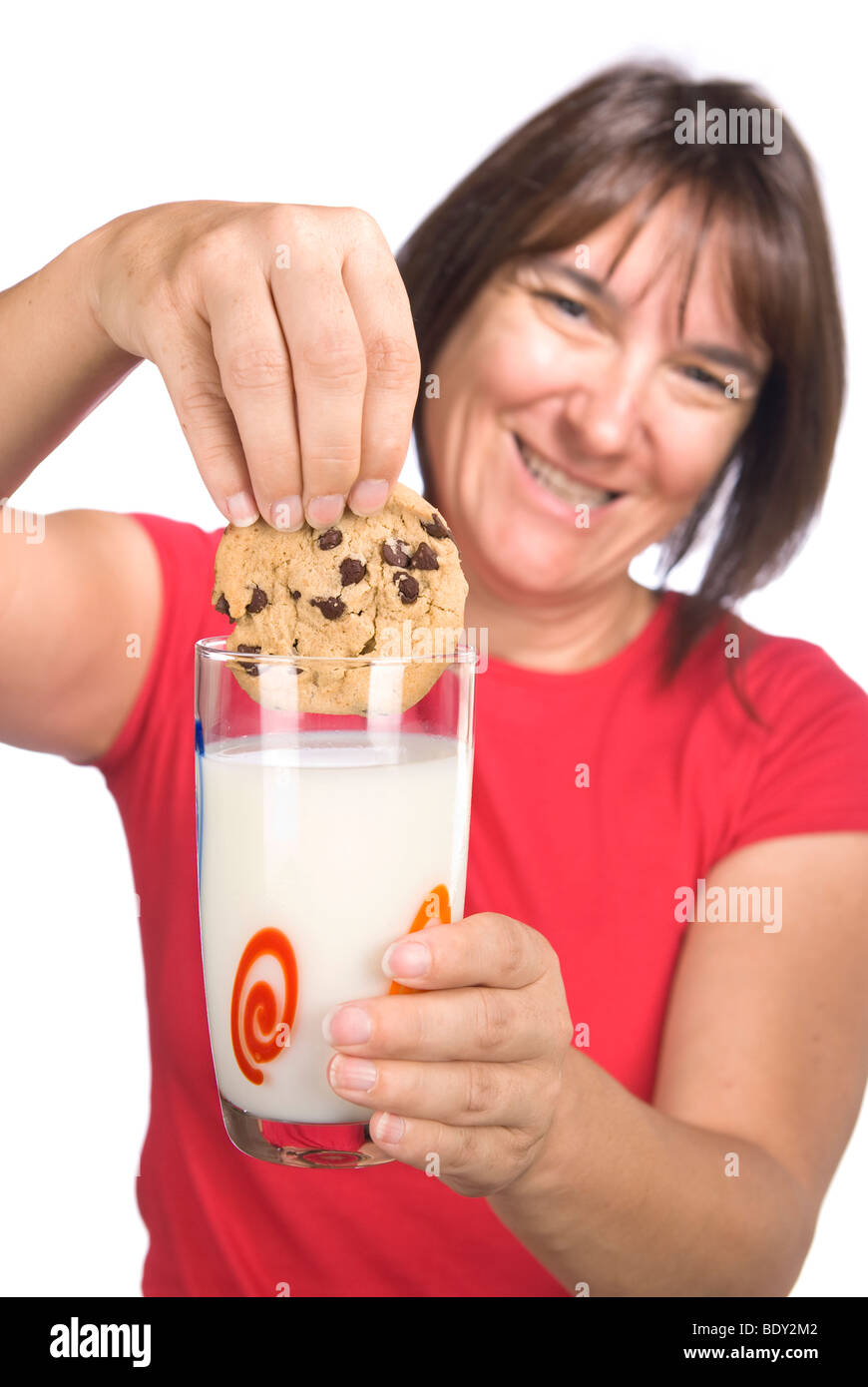 Una mujer felizmente mates su galleta de chocolate en un vaso de leche fría. Foto de stock