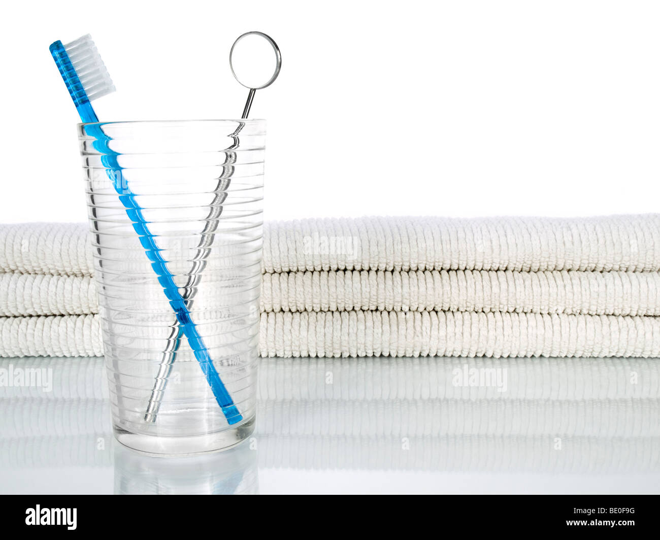 Un cepillo de dientes y una boca azul espejo en un vaso en un fondo con unas toallas. Foto de stock