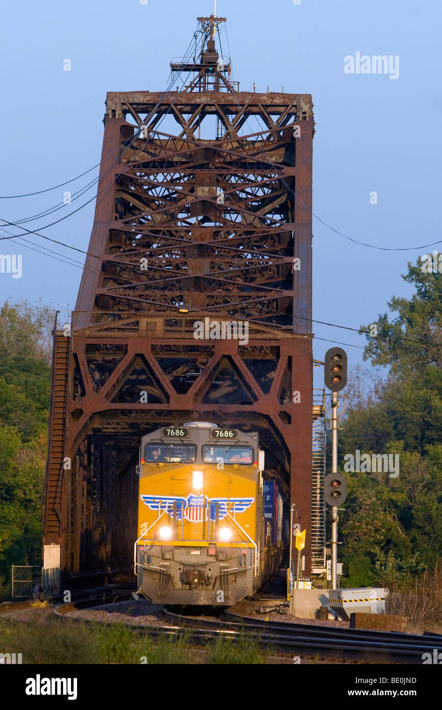 Partida hacia el oeste a la puesta del sol, una Union Pacific tren intermodal sale de su gigantesco Mississippi River Bridge. Foto de stock