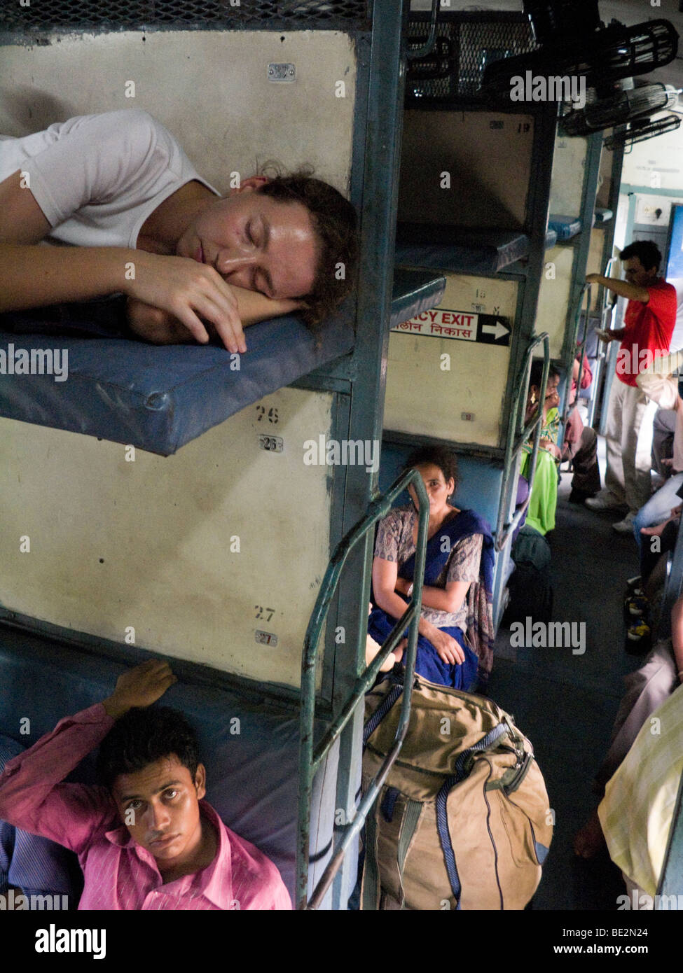 Pasajeros de Europa occidental descansa sobre una cama litera, sobre pasajeros indios sentados en un compartimiento del durmiente. Tren indio. Foto de stock