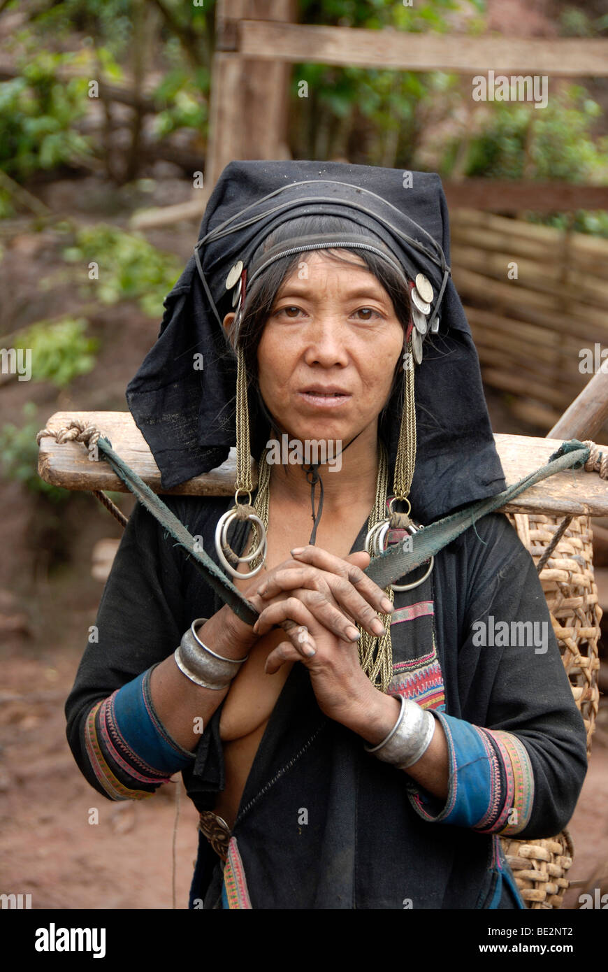 Retrato, etnología, mujer Akha Pixor grupo étnico en traje tradicional, capó como un tocado, llevando una cesta con yok Foto de stock