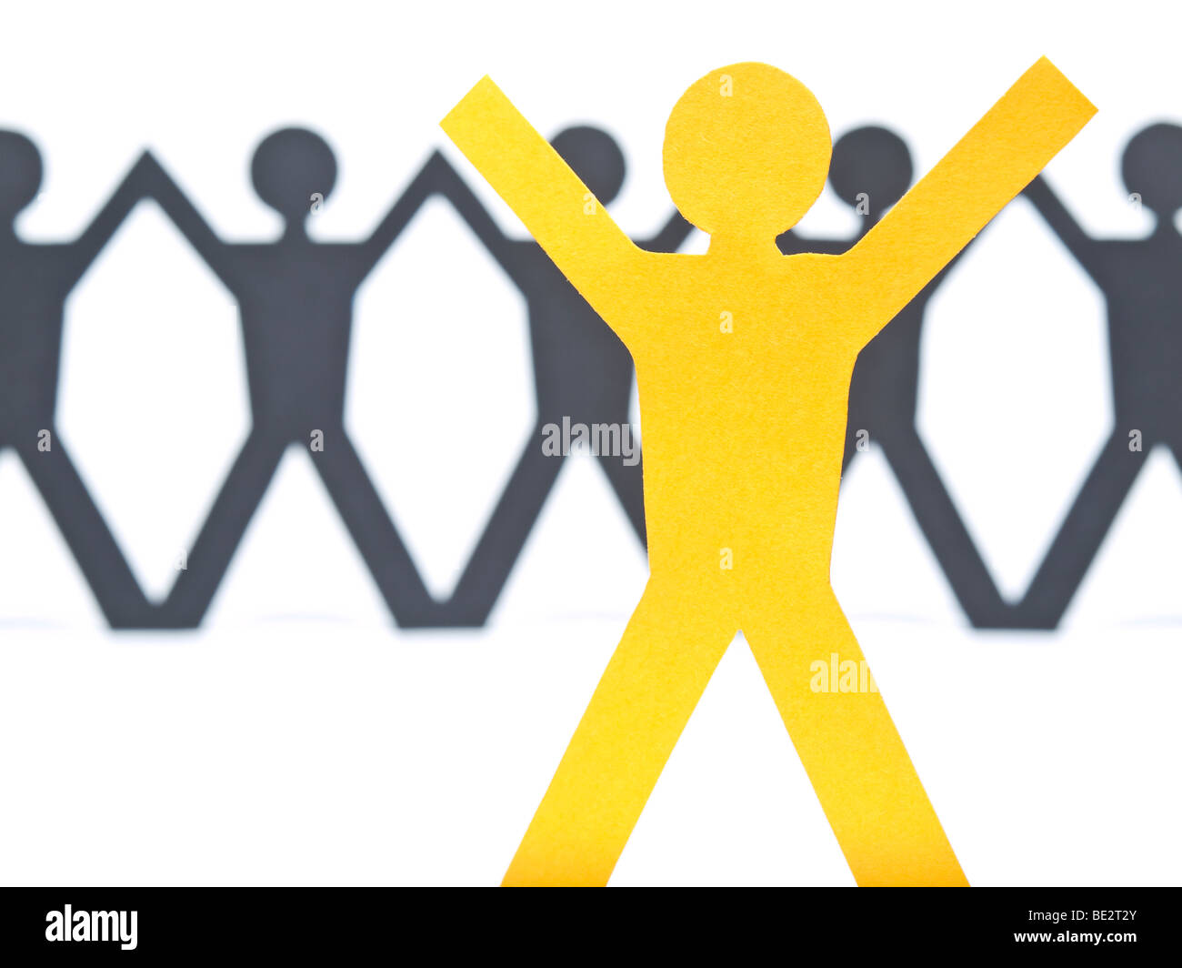 Un papel amarillo figura levanta los brazos. Una cadena de hombre de papel contra el fondo blanco. El enfoque selectivo en el primer plano. Foto de stock