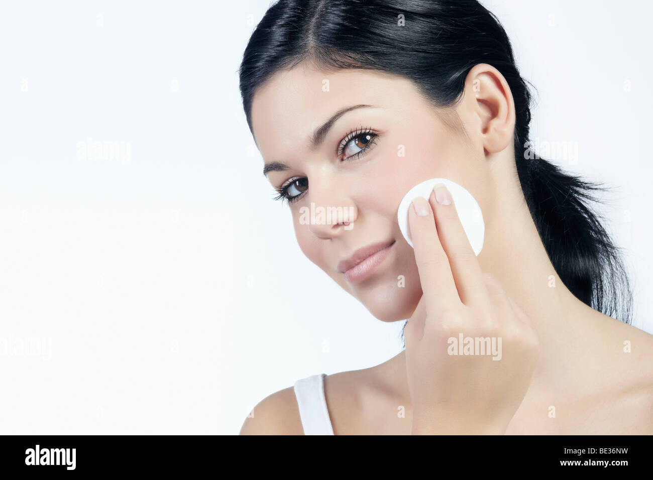 Mujer joven mirando hacia el espectador mientras se quita el maquillaje con una almohadilla de algodón, belleza Foto de stock
