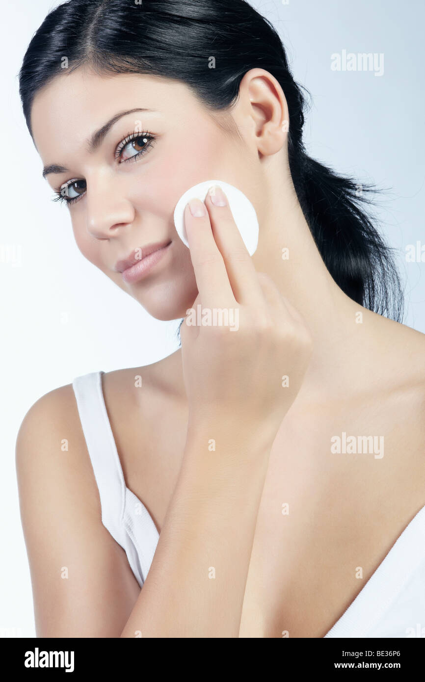 Mujer joven mirando hacia el espectador mientras se quita el maquillaje con una almohadilla de algodón, belleza Foto de stock