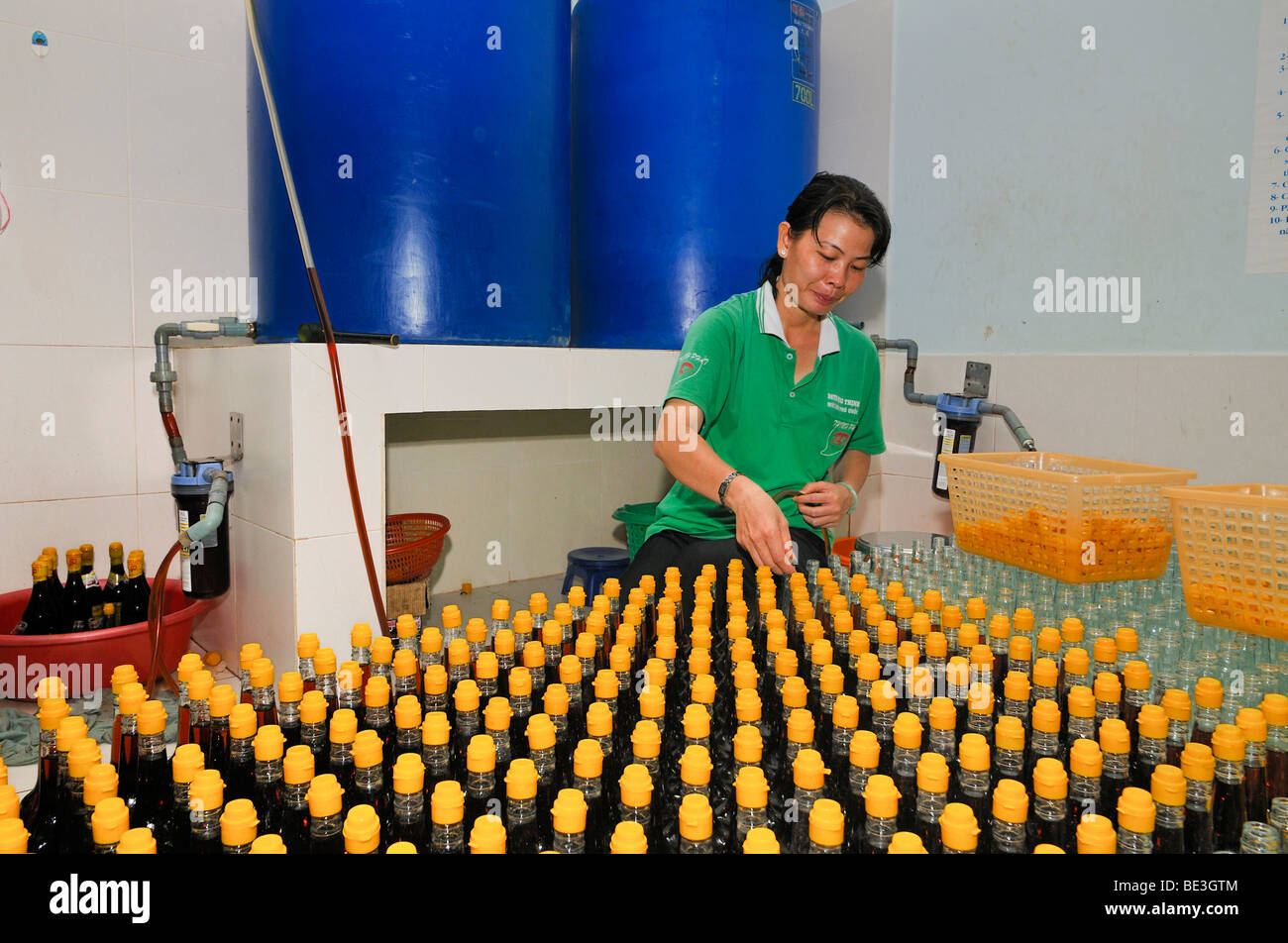 Mujer Vietnamita durante el embotellado de la tradicional salsa de pescado vietnamita Nuoc mam en botellas de vidrio con tapón de plástico amarillo Foto de stock