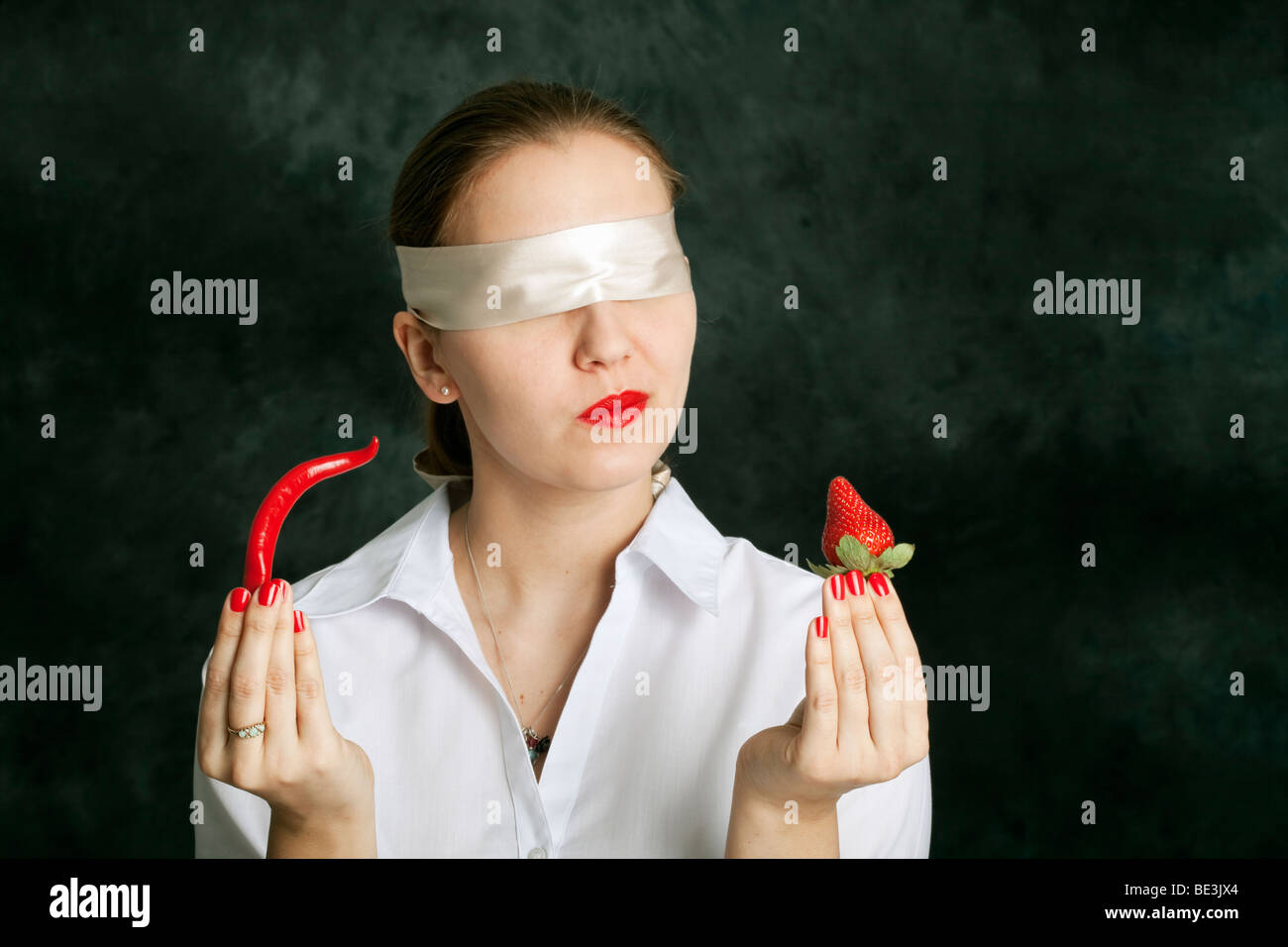 Mujer con los ojos vendados sosteniendo una guindilla y una fresa Foto de stock
